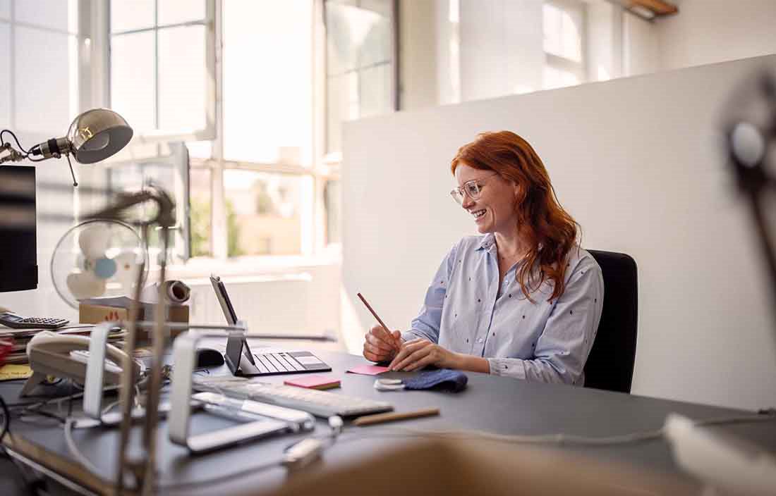 Businessperson with red hair sitting at their desk using a portable two-in-one laptop device.