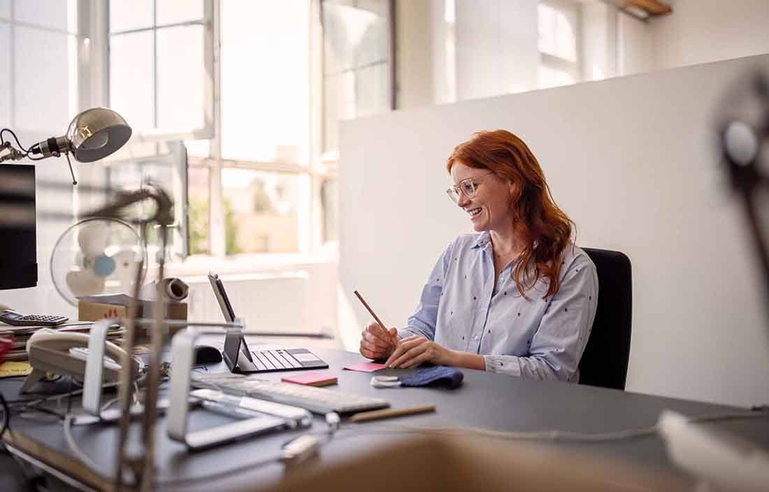 Businessperson with red hair sitting at their desk using a portable two-in-one laptop device.