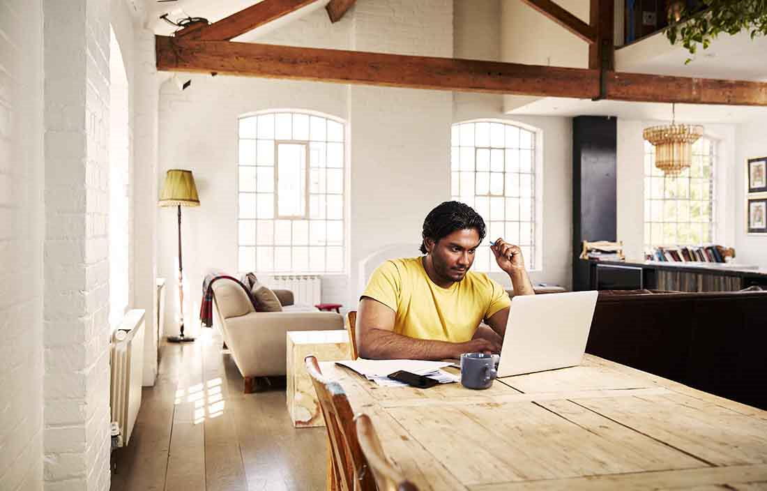 Man sitting at home in a kitchen using a laptop computer.