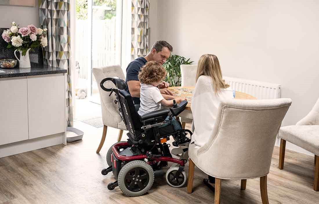 Parents sitting at a table with their child in a motorized wheelchair