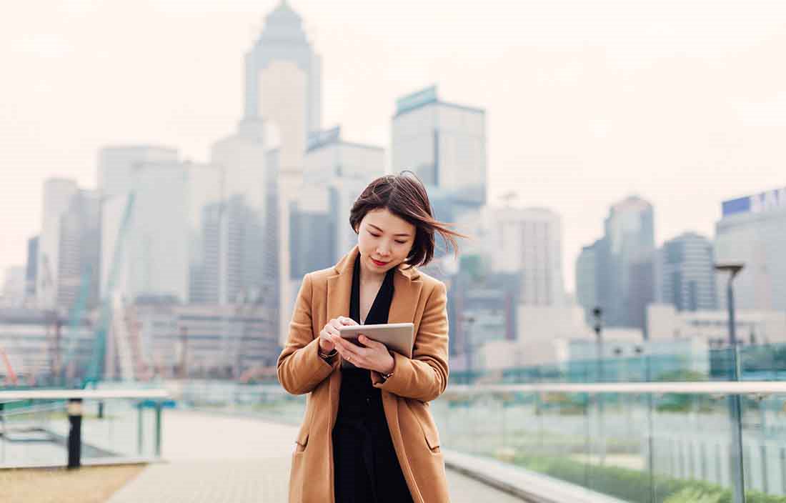 Businesswoman standing in a park area using a handheld tablet.