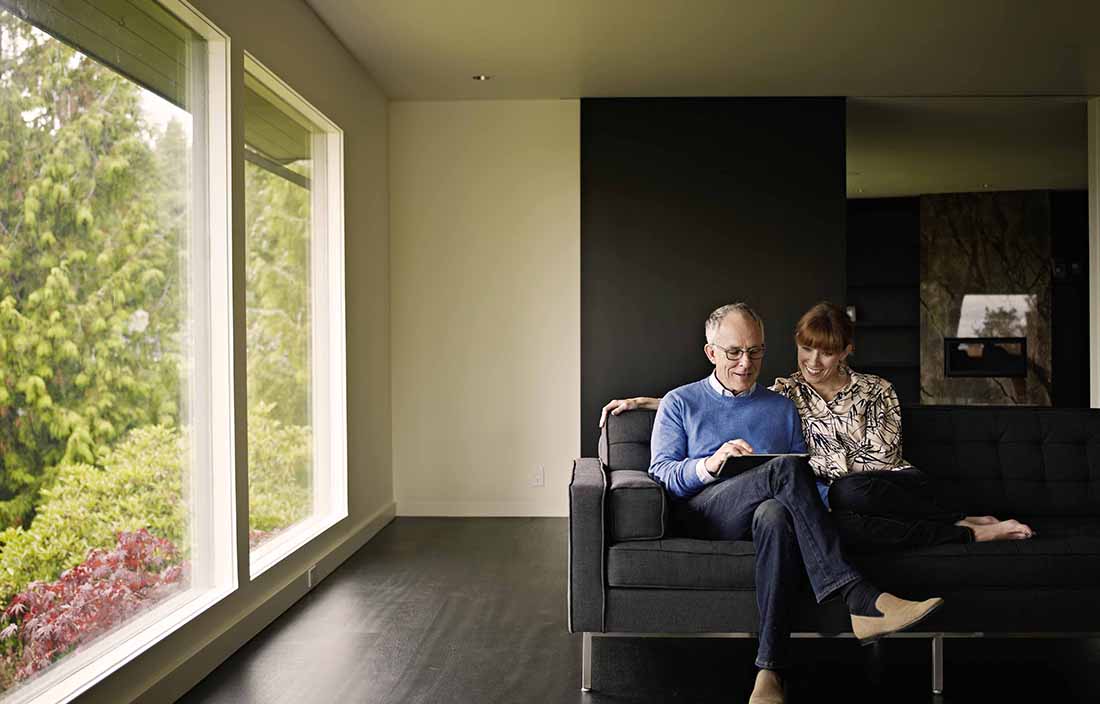 Middle-aged couple sitting on a couch using a handheld tablet together.