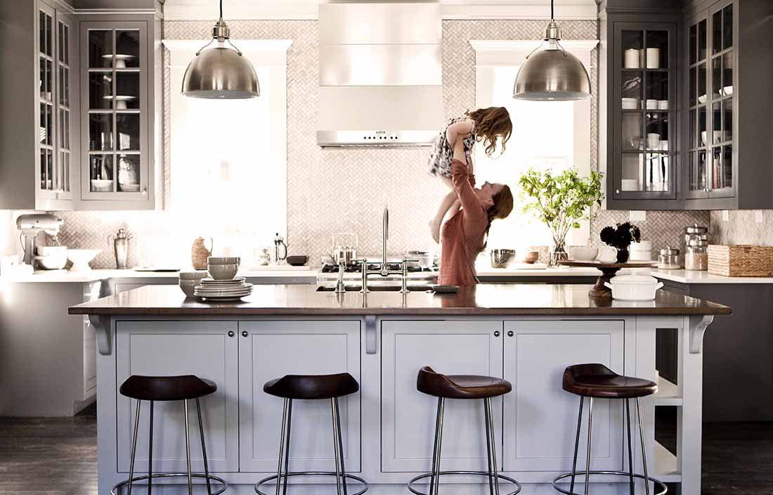 Mom in a kitchen holding up her daughter in the air.