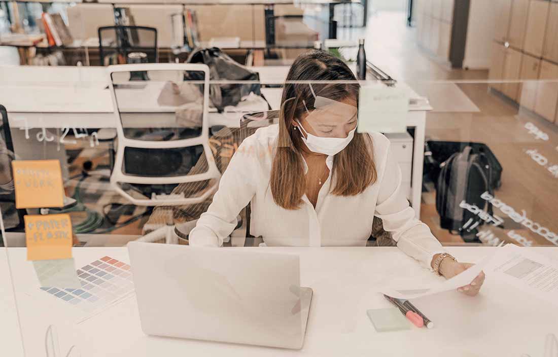 Businesswoman wearing a protective face-shield at her office desk.