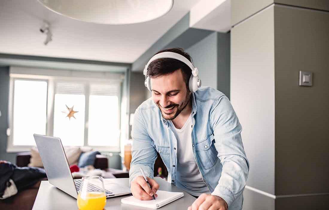 Man wearing headphones standing at kitchen island with laptop computer on top of it.