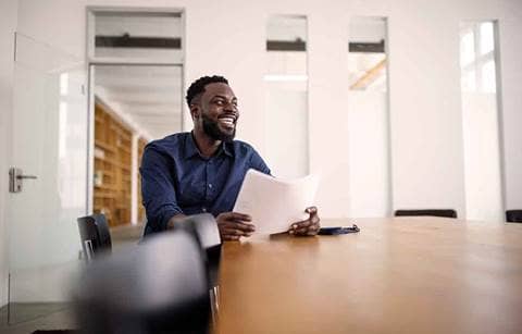Business professional sitting at a conference room table holding a piece of paper and smiling.