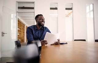 Business professional sitting at a conference room table holding a piece of paper and smiling.
