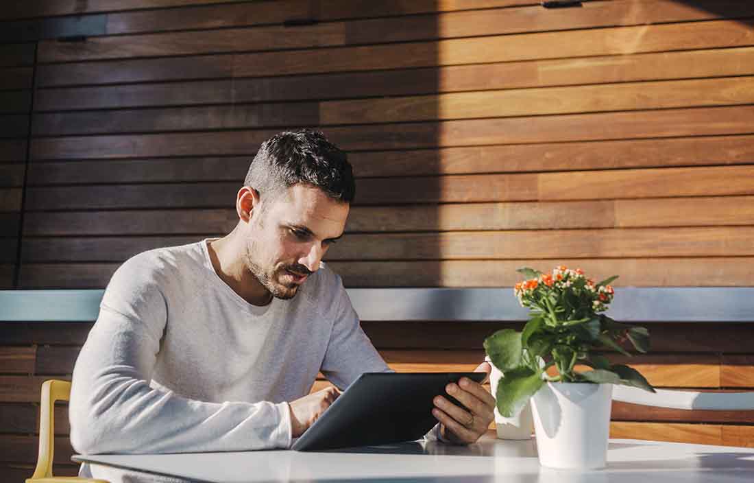 Business professional using a handheld tablet while sitting at a cafe table.