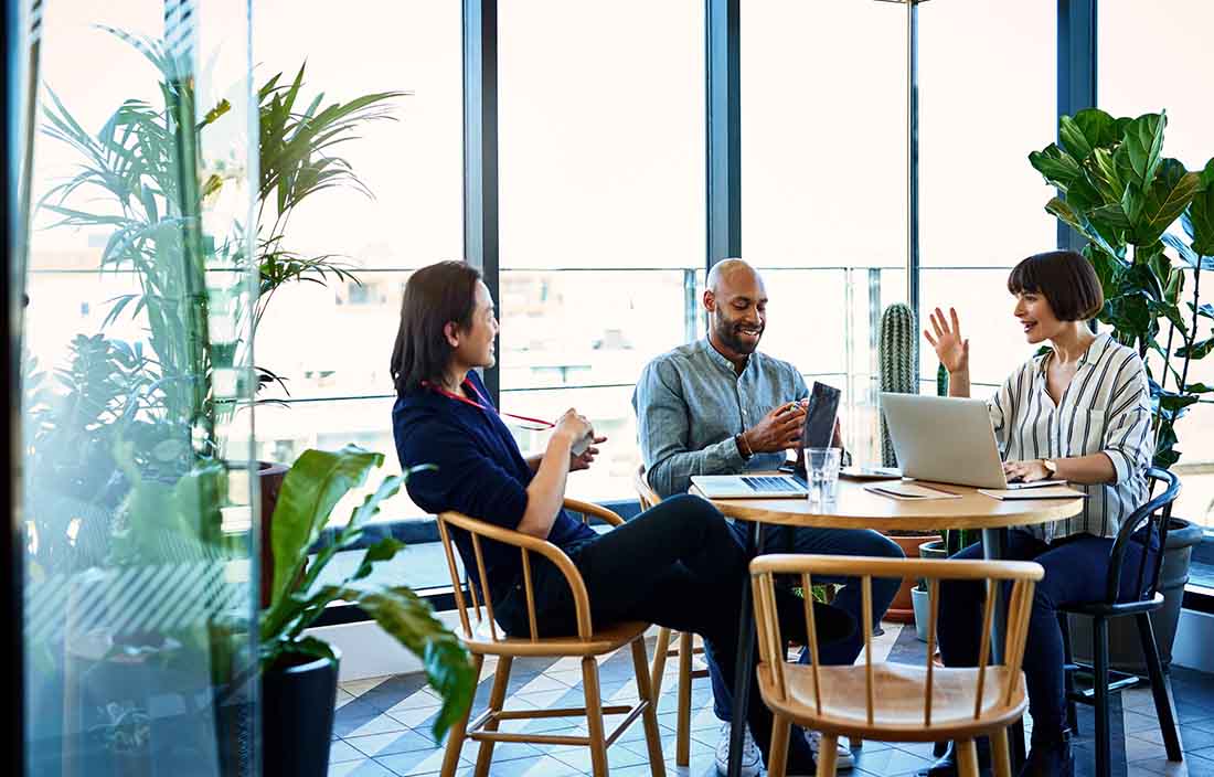 Business professionals sitting at a cafe/break table having an impromptu meeting with their laptops out.