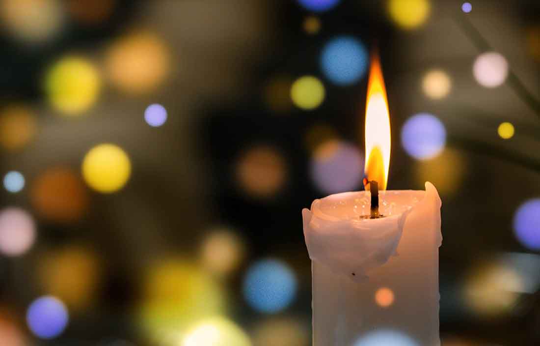 Close-up view of a candle with lights in the background.