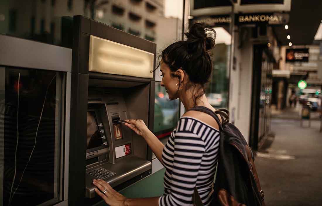 Younger adult using an ATM machine on the street to withdraw money.