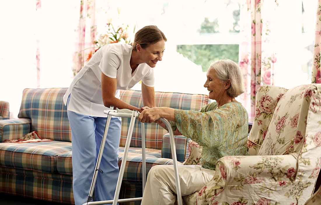 A senior care nurse helping an elderly patient with their walker.