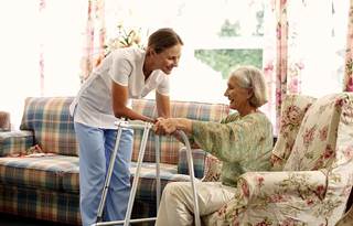 A senior care nurse helping an elderly patient with their walker.