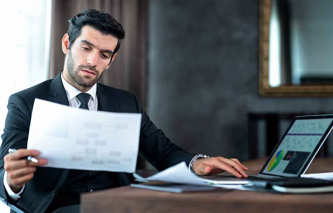 Business professional examining a paper document while also using their laptop computer.