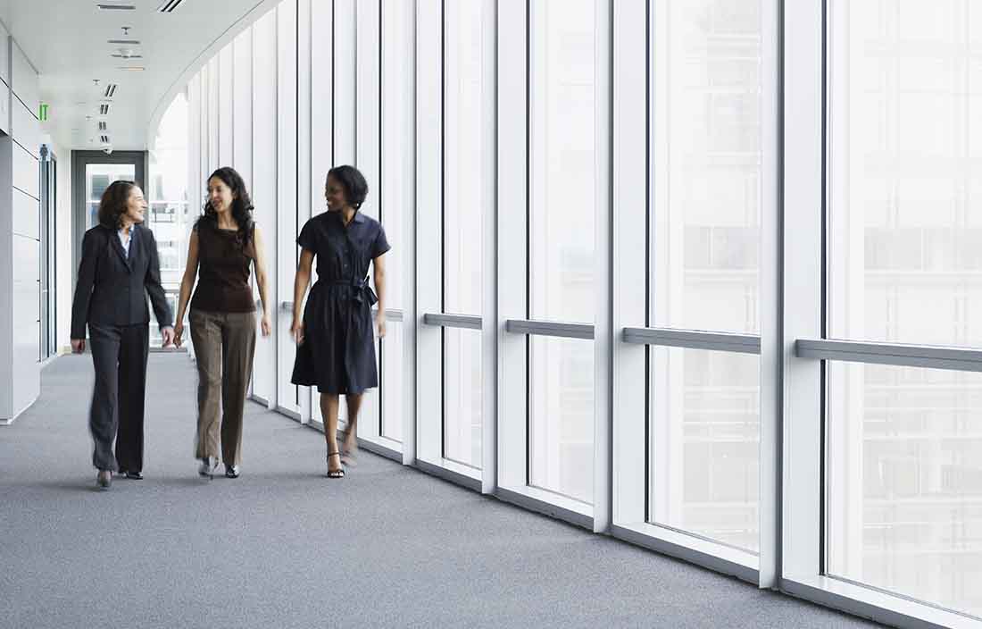 Three business professionals walking down a hallway talking to each other.