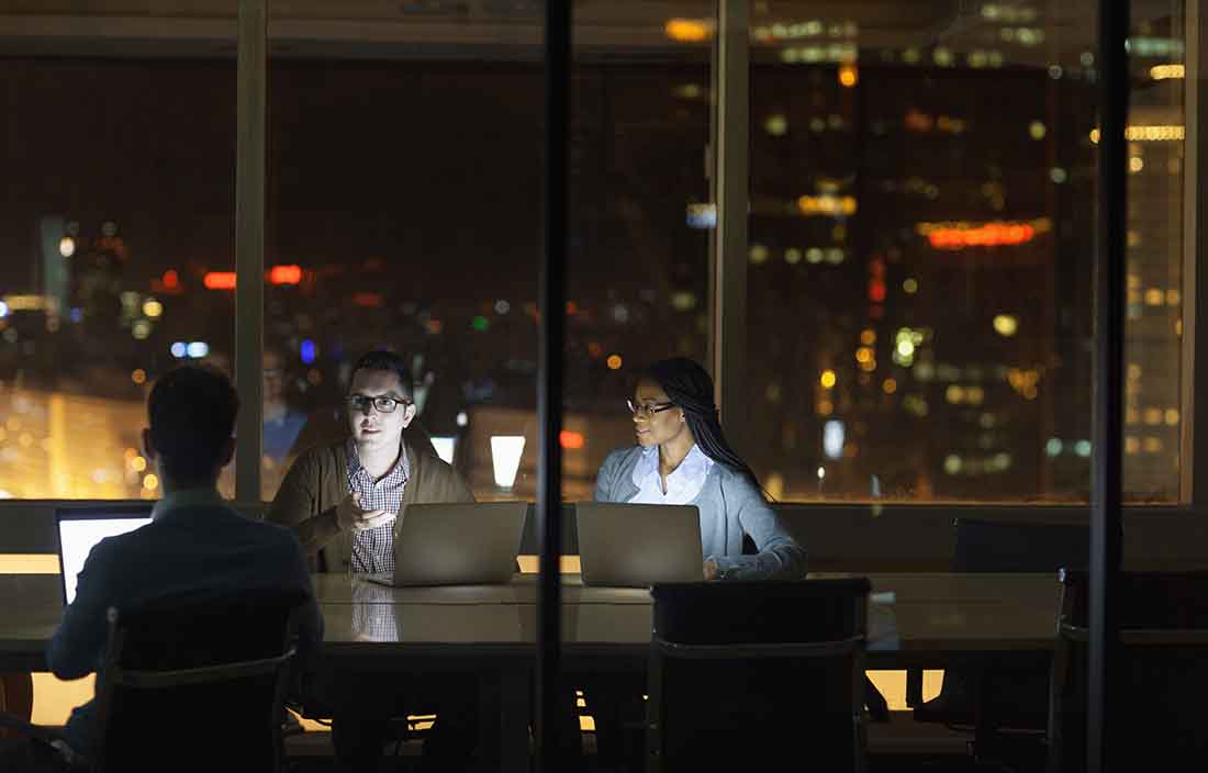 Three analytics professionals working on their laptops late at night.