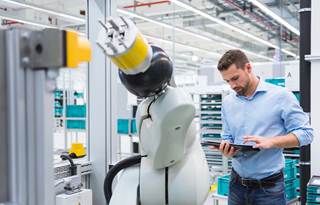 Business professional in casual clothing standing next to an automated robot.