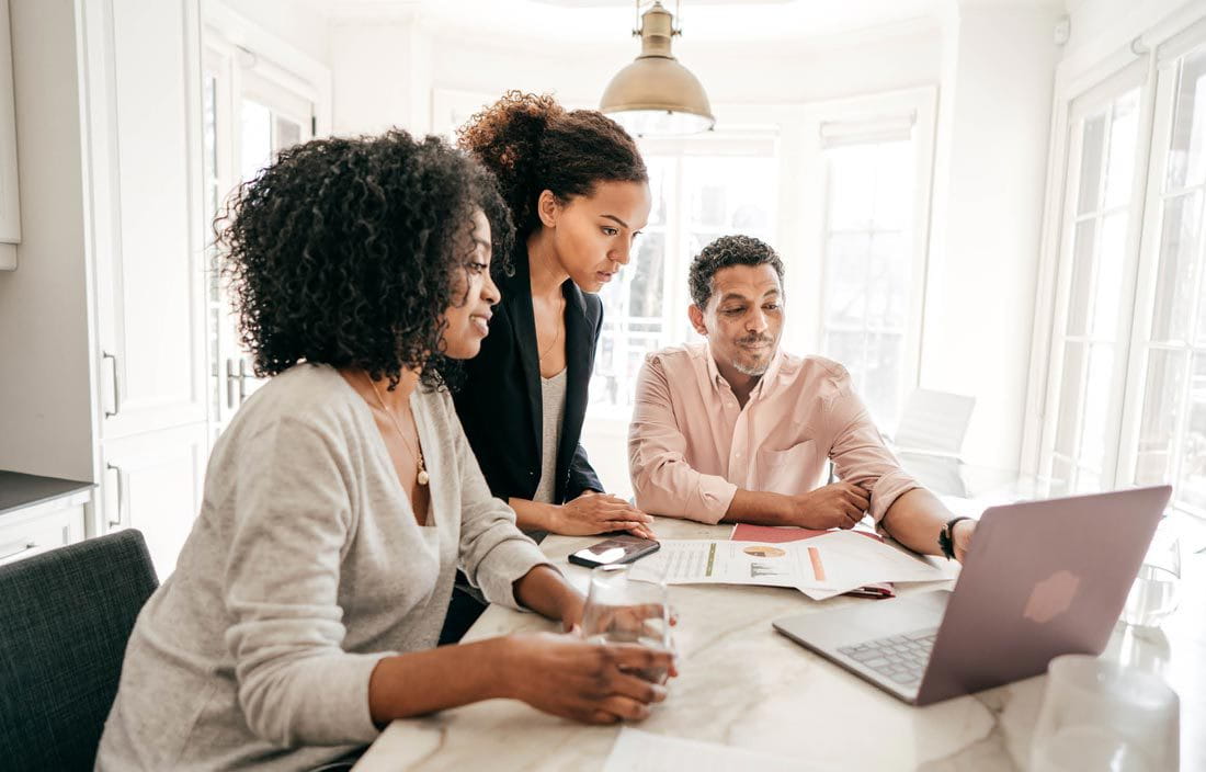 Family huddled around a laptop computer at a kitchen table.
