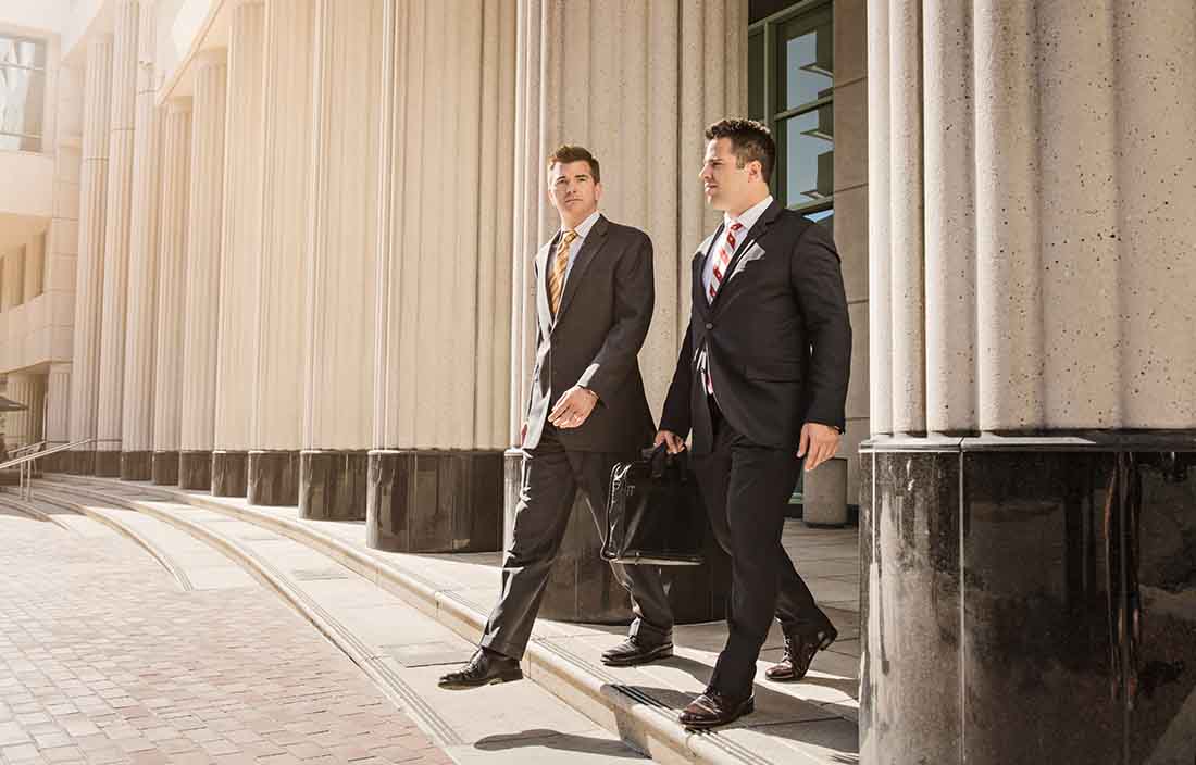 Two business professionals walking next to a building with big marble columns.