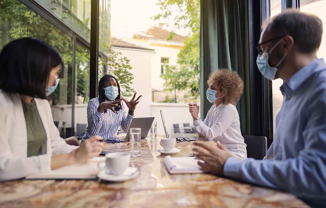 A group of business professionals having a meeting wearing protective facemasks.
