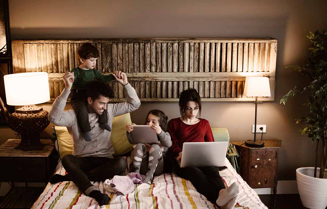 A family sitting in bed together using laptop computers.