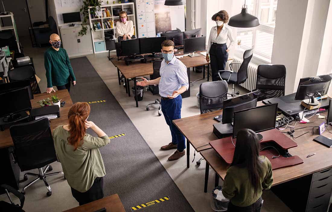 Business professionals standing in an office while wearing protective facemasks.