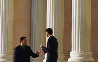 Two business professionals in suits outside a courthouse talking.