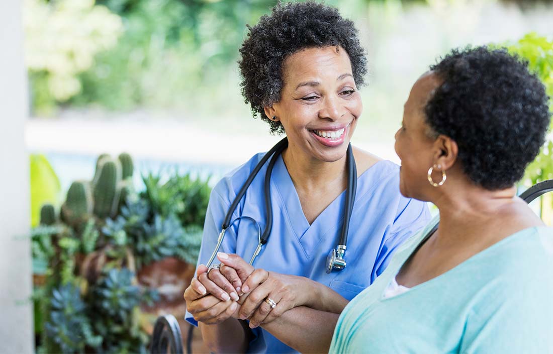 Healthcare worker sitting with a middle-aged patient holding their hand and smiling.