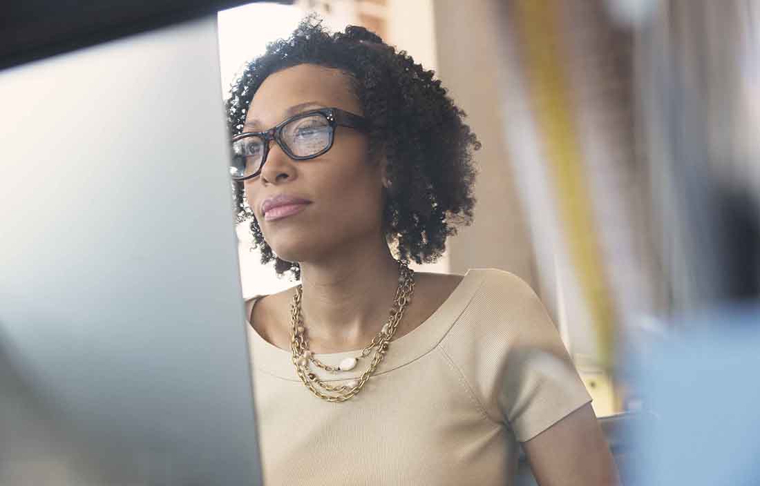 Business professional wearing a necklace and glasses using a desktop computer.