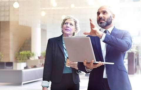 Business professional holding a laptop while explaining something to another colleague.