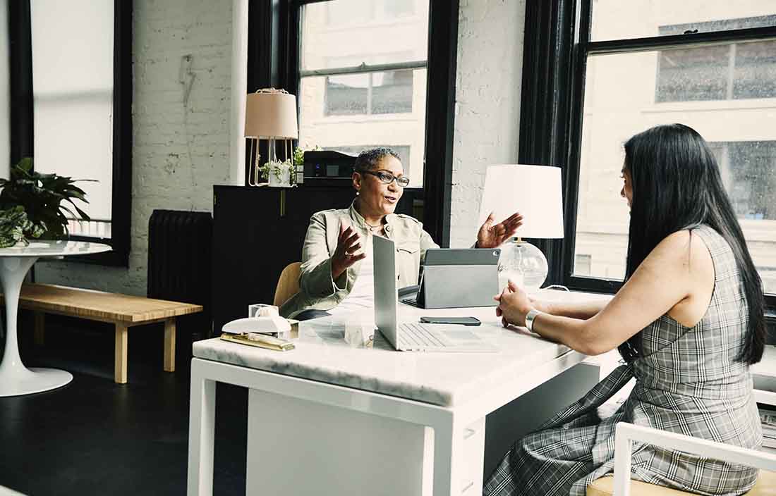 Two business professionals discussing with one another at a desk.