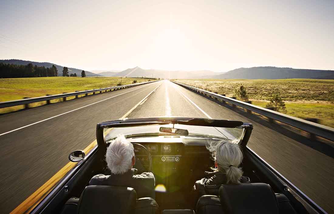 Car driving down the road with the sun on the horizon.
