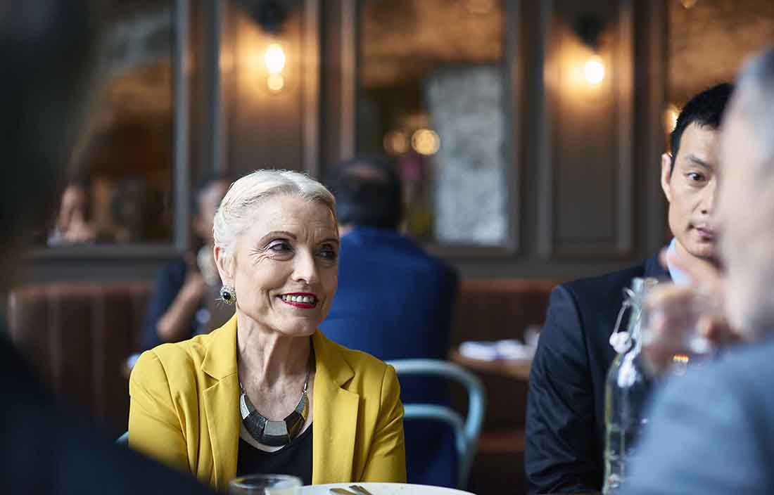 Photo of elderly woman smiling while sitting at a restaurant.