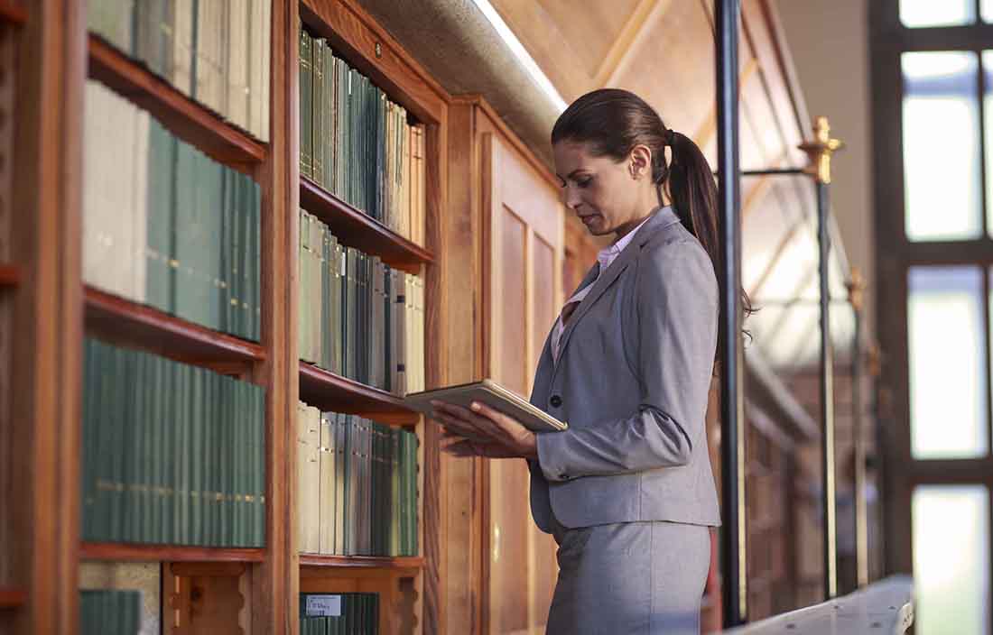 Business woman looking at a book she selected from a shelf of books.