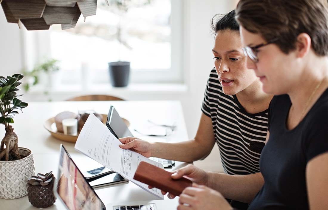 Two people checking documents and looking at a laptop computer screen.