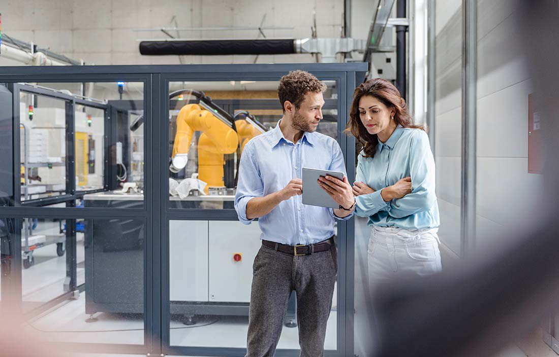 Business professionals looking at a tablet handheld while on a manufacturing floor.