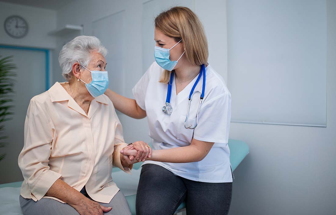 Nurse with face mask on assisting a senior patient.
