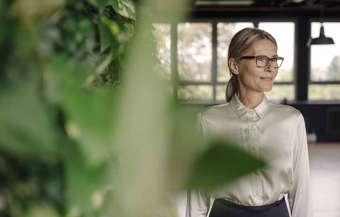 Middle aged woman standing next to a plant.