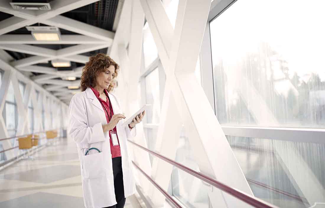 Medical doctor reading on their tablet computer in a hospital hallway.