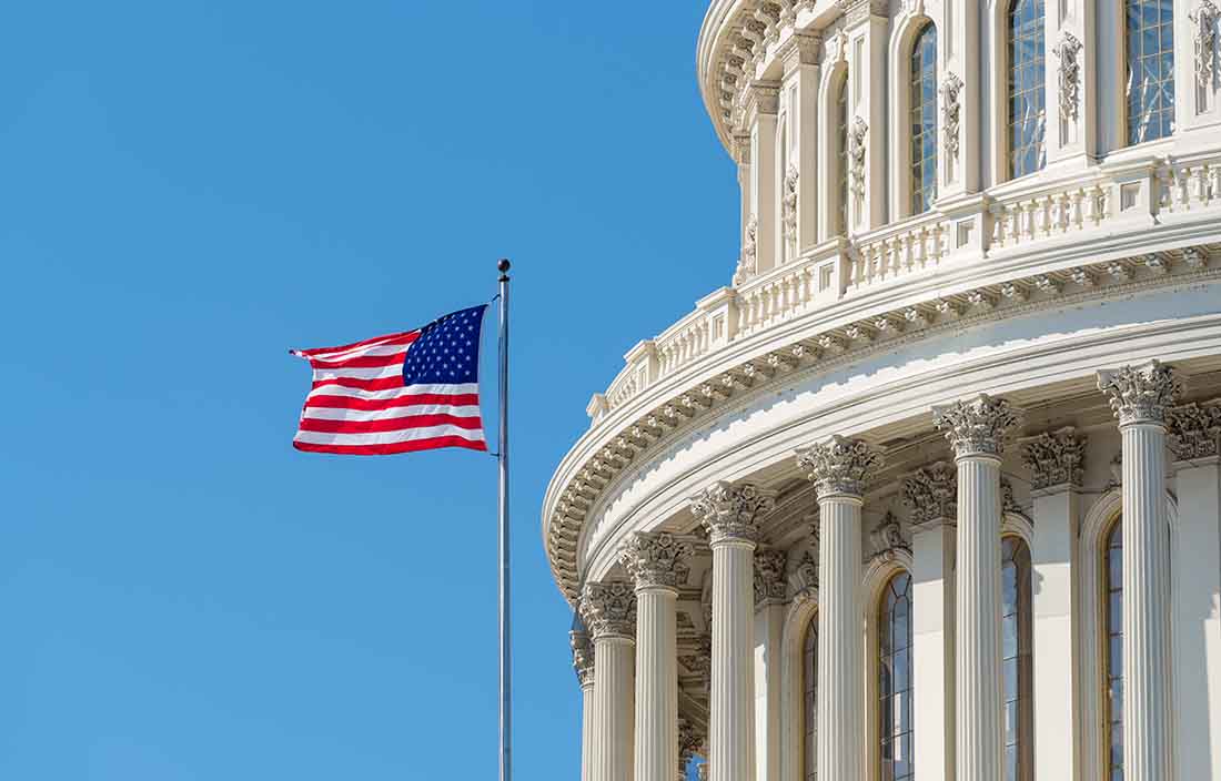 U.S. flag flying in front of Capitol building.
