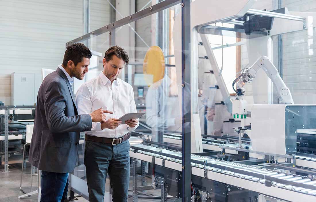 Two business professionals looking at their tablet computer in a manufacturing facility.