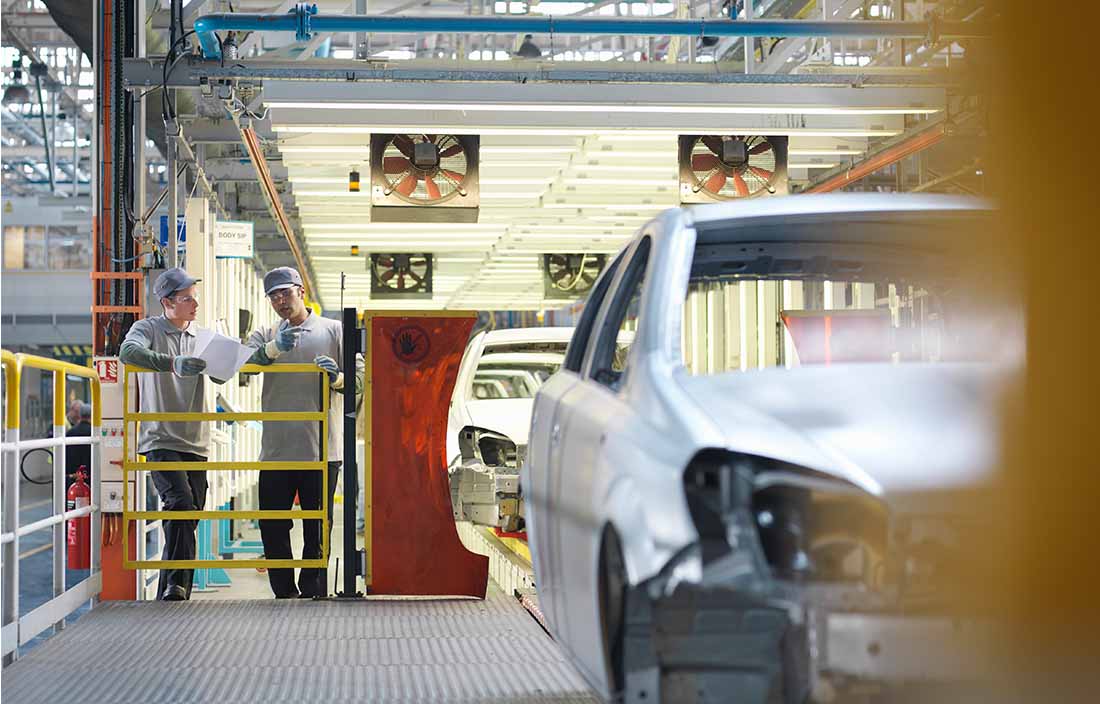 Two factory workers discussing vehicle assembly.