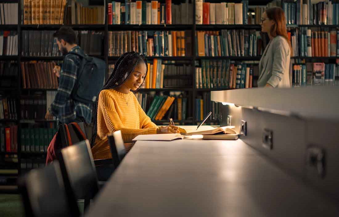 Student sitting at a desk in a library doing homework.