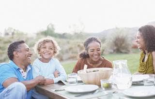 Multiple generations of a family laughing and eating dinner together.