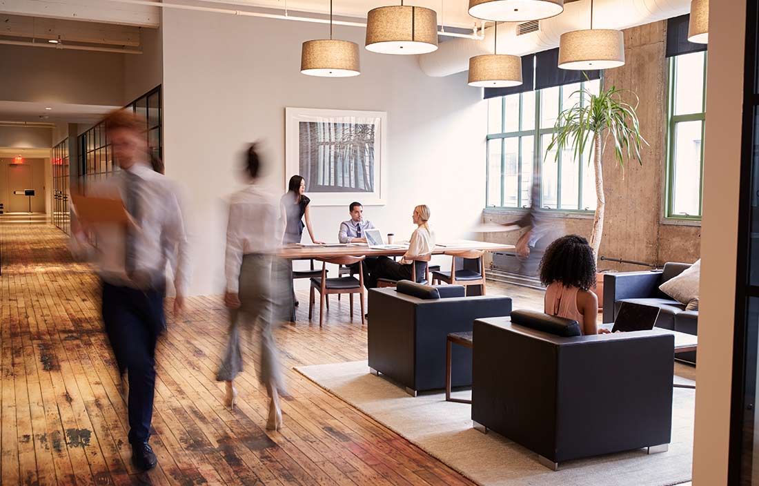 Image of a bustling modern office, with various seating options and staff doing in-person work.