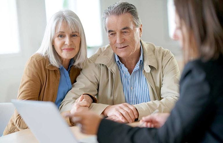 A couple smiling and looking at a financial advisor's paper.