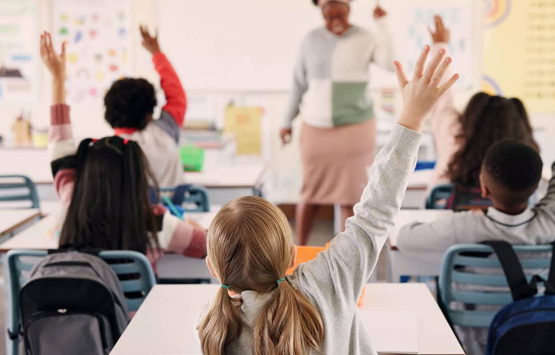 Kids raising their hands in a classroom.