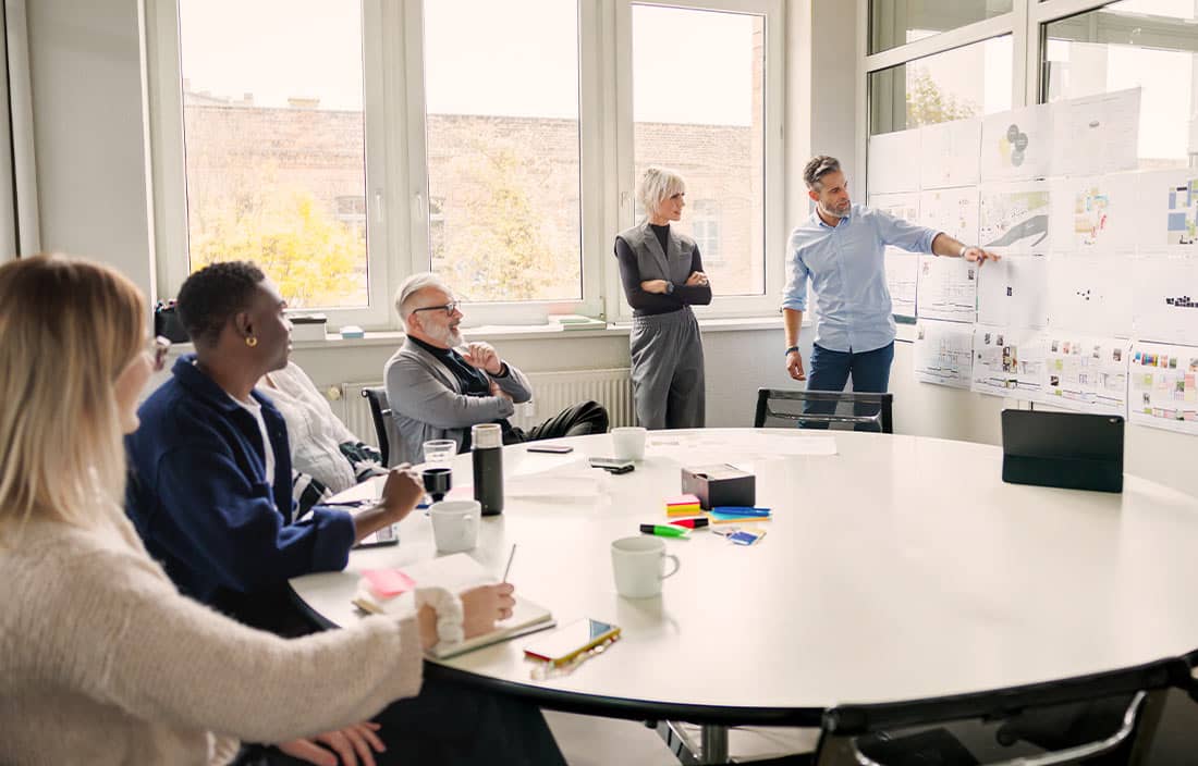 A group of people in an office watching a colleague present data on a whiteboard.
