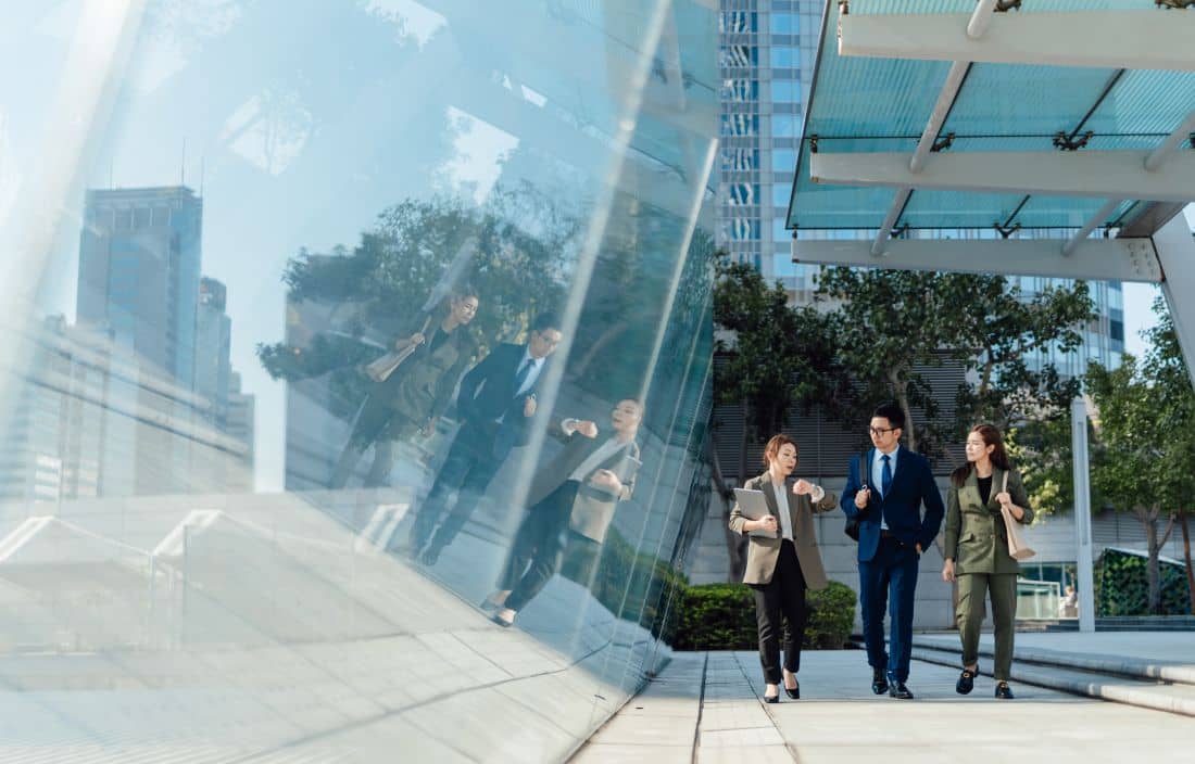 Three business professionals talking while walking outside a modern office building.