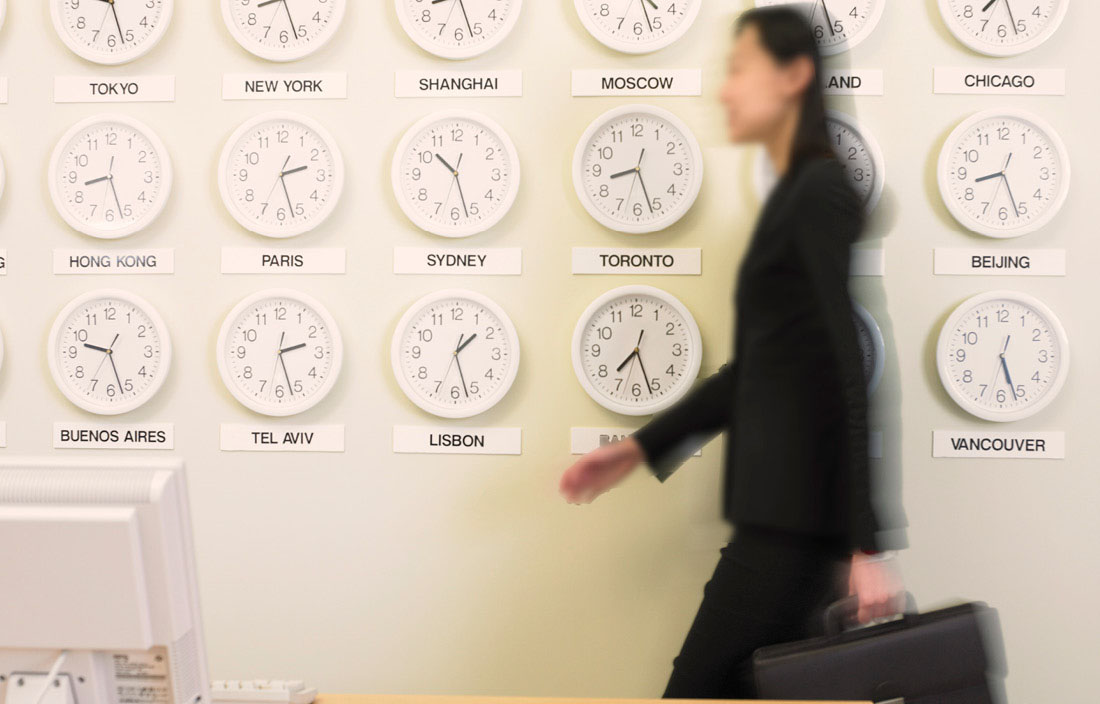 Japanese business woman walking past a wall with international clocks.